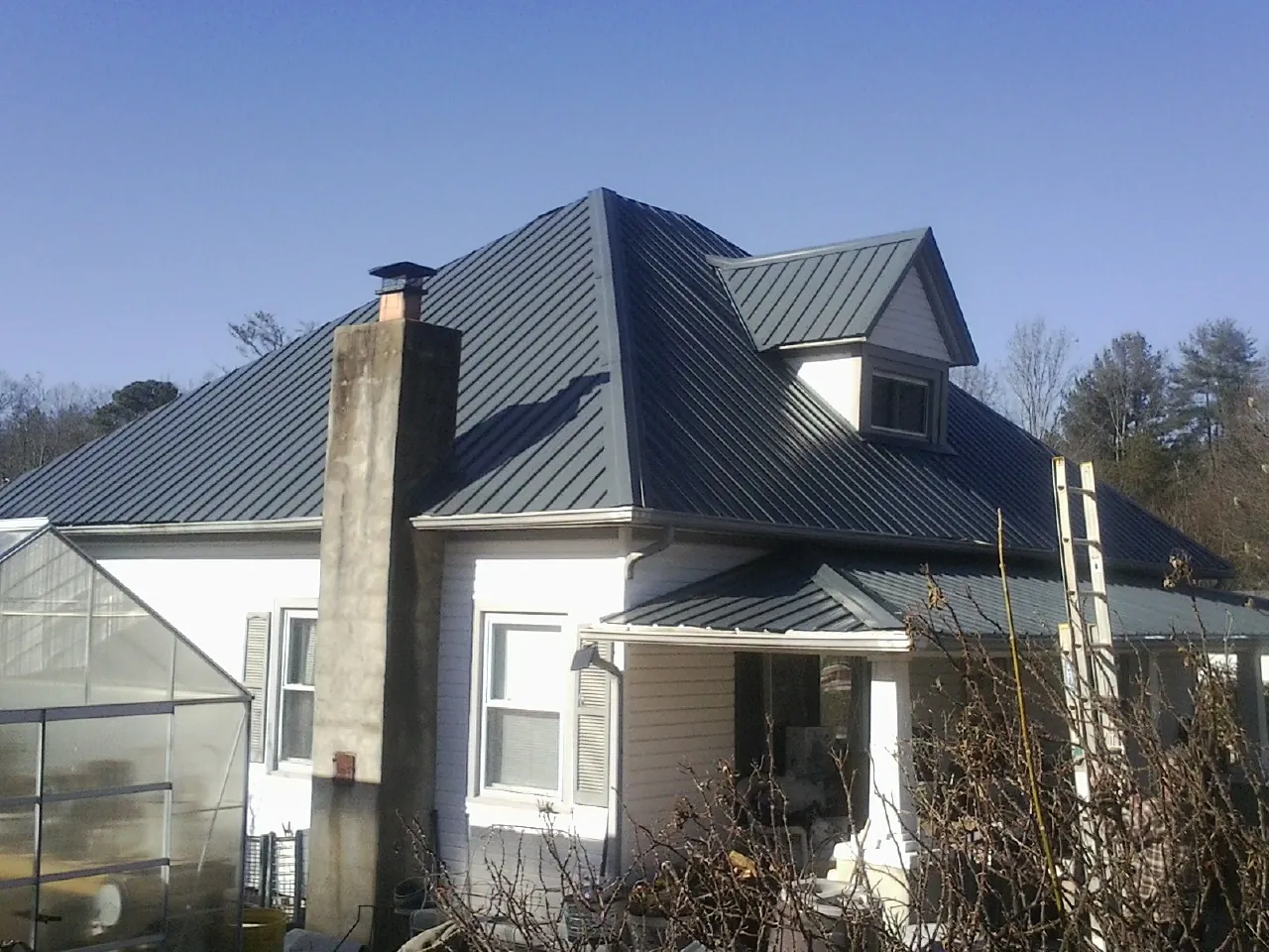 Dark blue standing seam metal roof on a white farmhouse with dormer — Slate & Tile Roof Repair by Roofing Brothers in Ashburnham