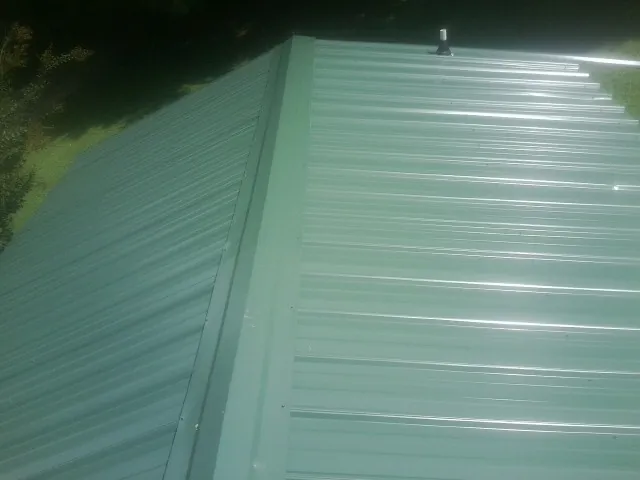 New green metal panels meeting at the ridge of a roof — Flat Roof Repair work by our crew in Ashburnham