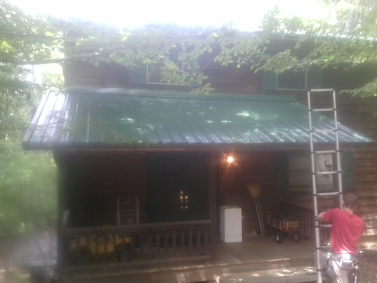 Worker on a ladder at the green porch roof of a wooded cabin in Ashburnham