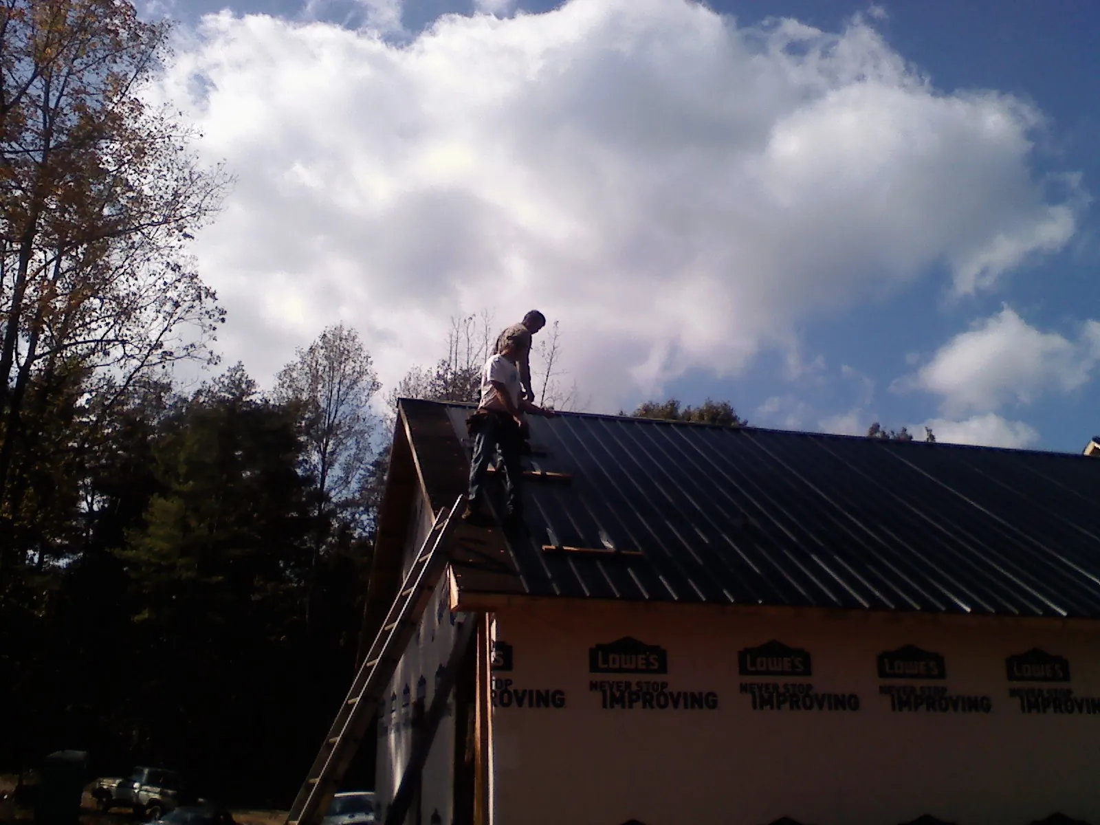 Roofer fastening dark metal panels high against a cloudy sky, from a Roof Inspection job in Ashburnham